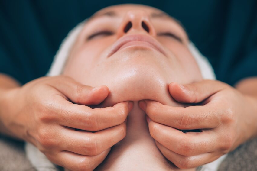 Close-up of a young woman receiving chin and jawline face lifting massage